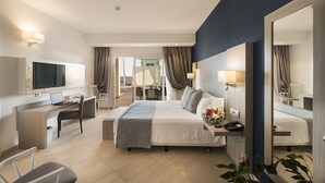 A modern hotel room with a large bed, a desk with a laptop, a flat-screen TV mounted on the wall, and a large mirror. - Royal Palm Resort & Spa - Adults Only (Pajara)