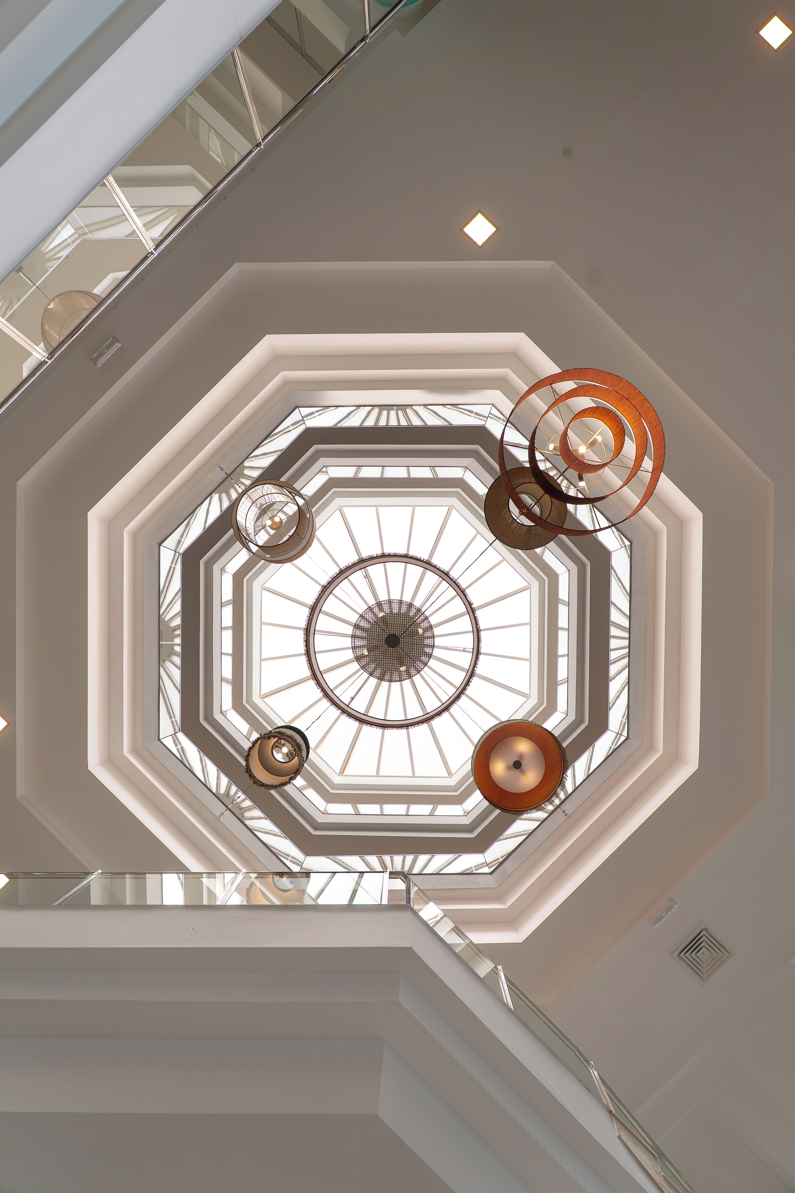 Een meerlaags atrium met een dakkoepel en moderne verlichtingsarmaturen.