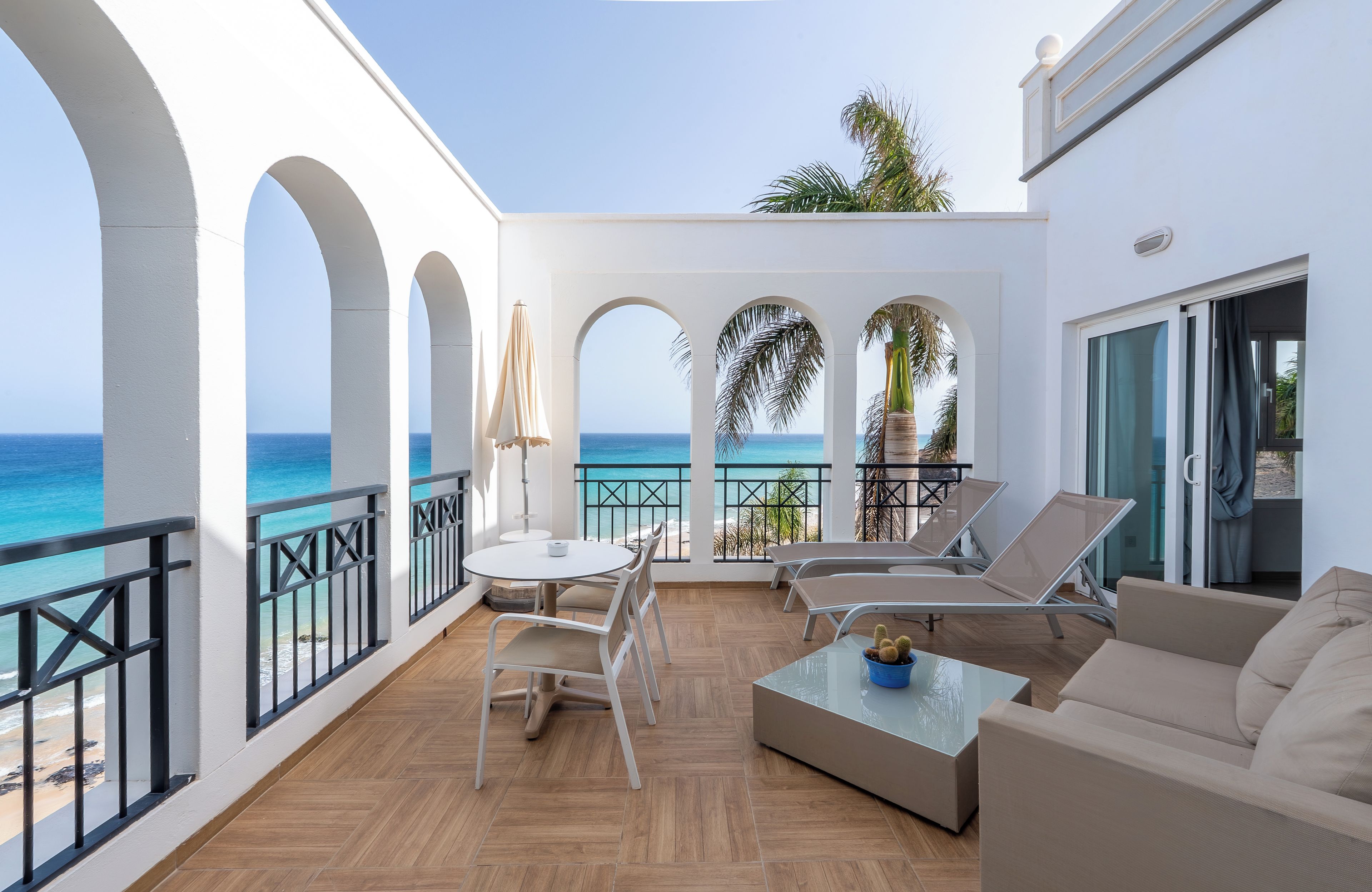 A balcony with a view of the sea, furnished with a table, chairs, and a sofa.