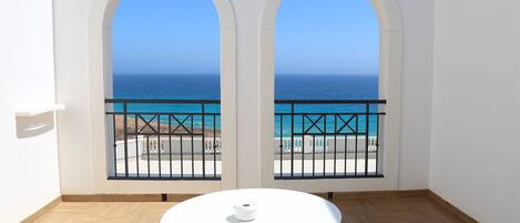 A balcony with a view of the ocean, a round table, and two chairs.