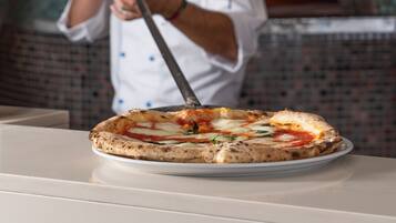 Un chef con uniforme blanco y gorro de cocinero, sosteniendo una pala para pizza frente a un horno de ladrillo.