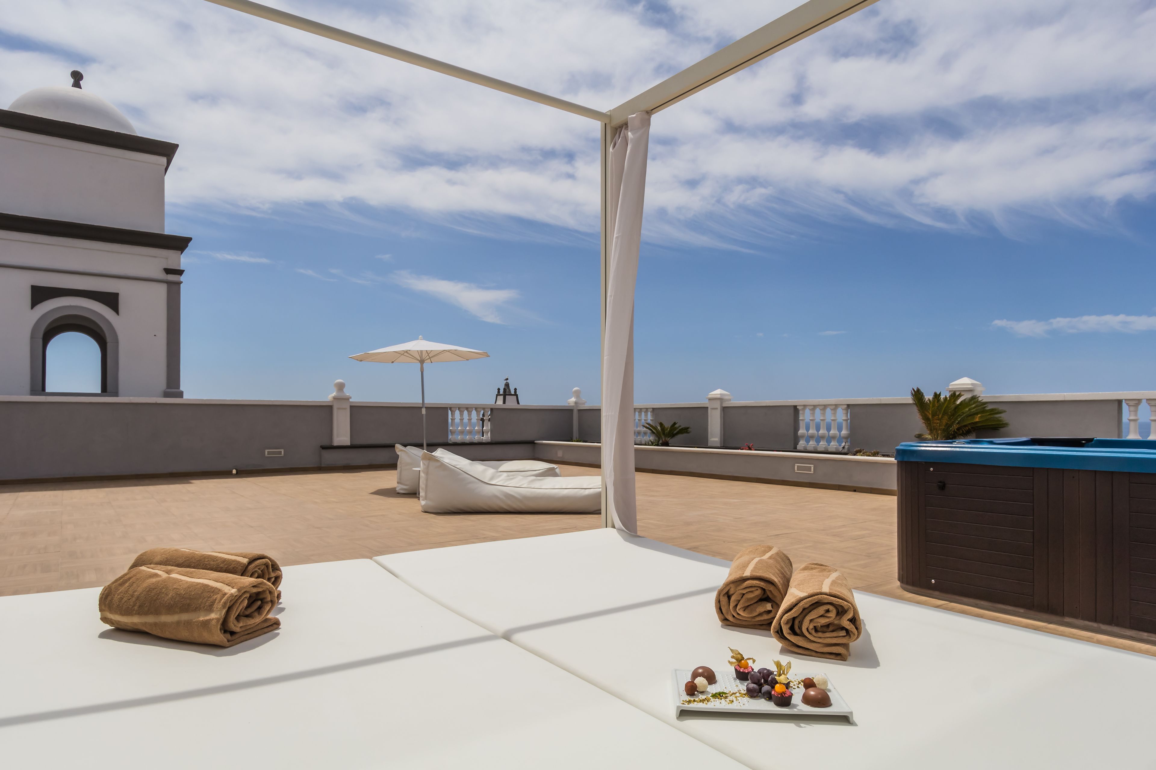 A rooftop terrace with lounge chairs, a hot tub, and towels.