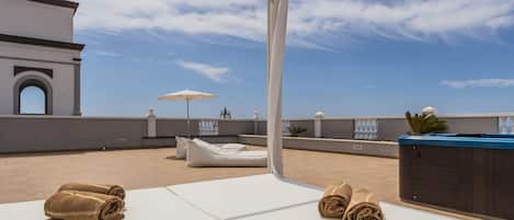 A rooftop terrace with lounge chairs, a hot tub, and towels.