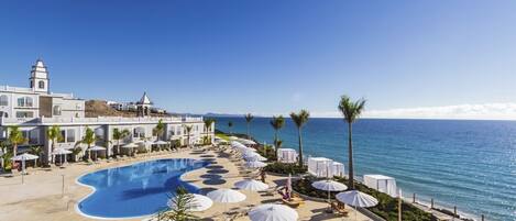 A resort with a large pool, beach chairs, umbrellas, and a view of the ocean.
