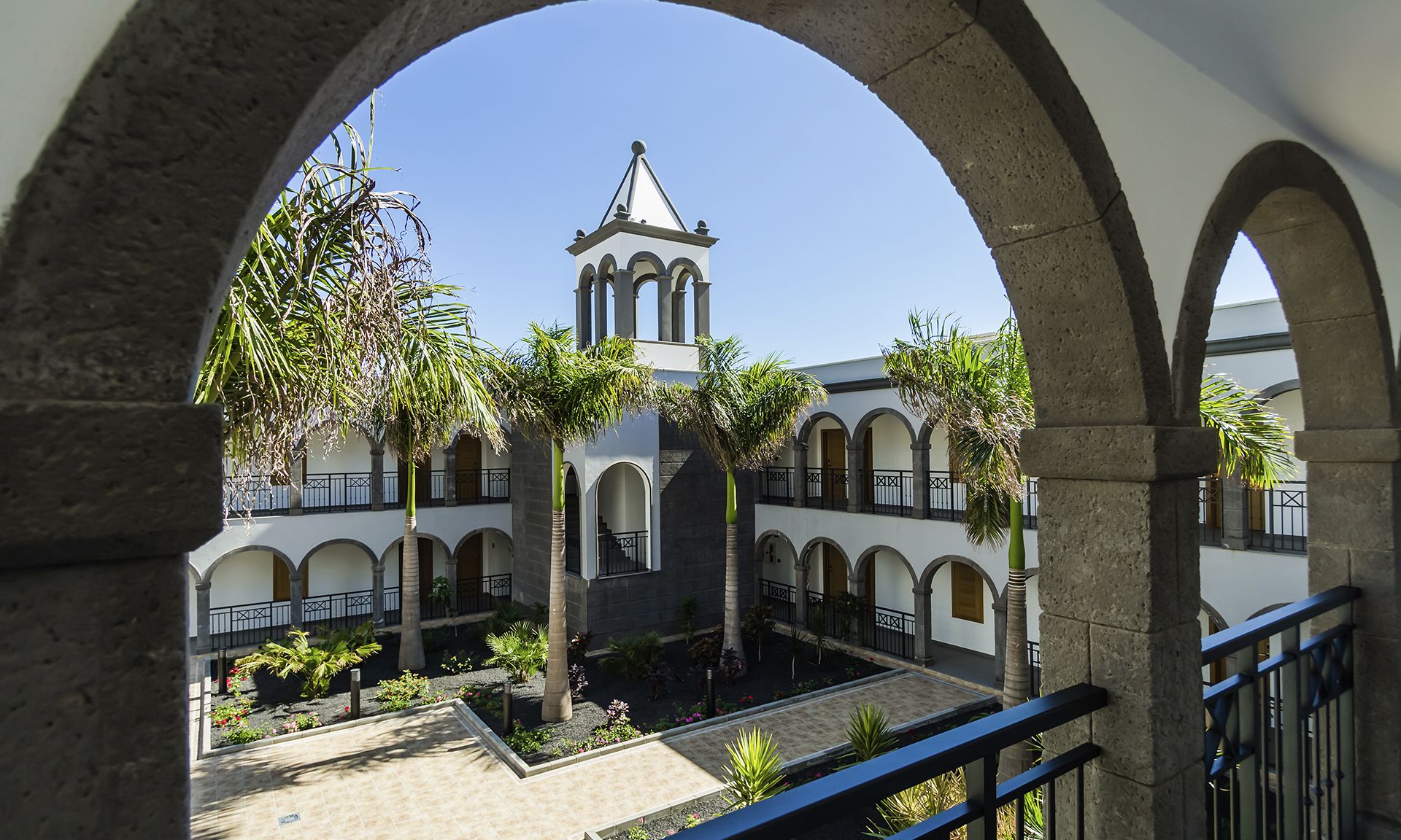 A courtyard with arches, palm trees, and a building with a bell tower.