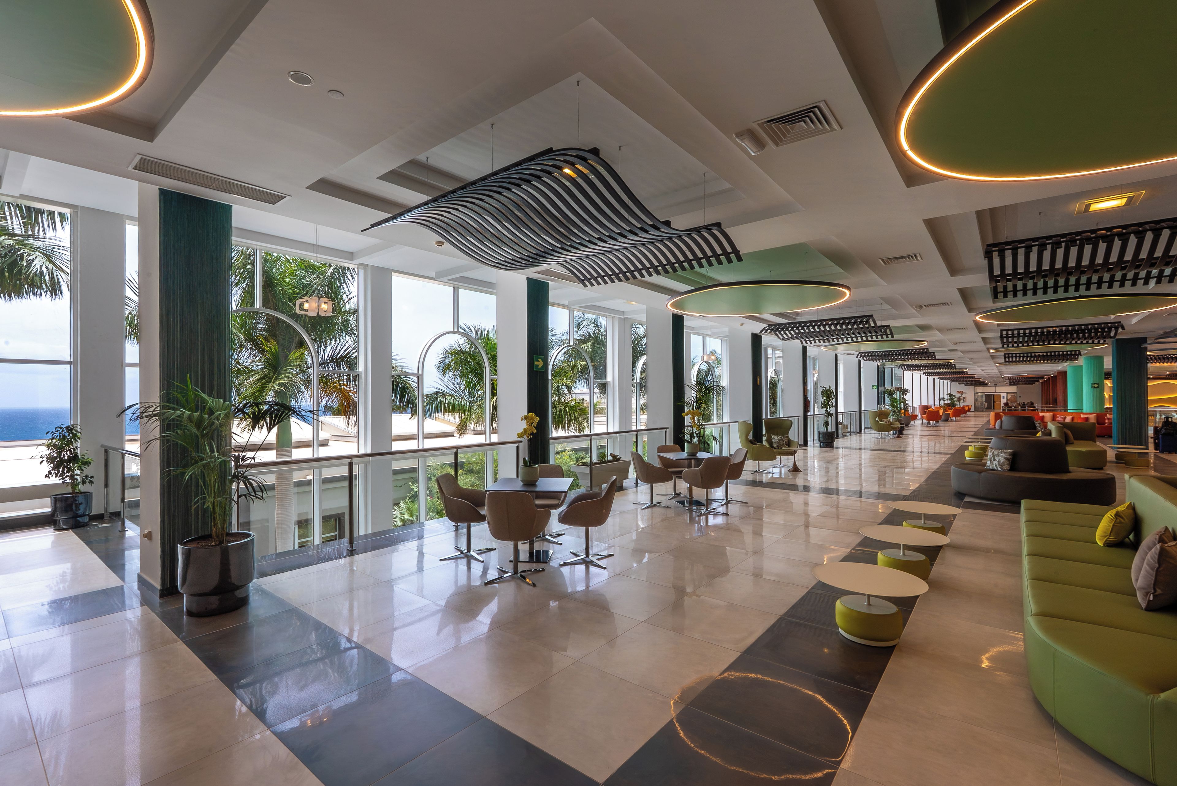 A spacious lobby with a modern design, featuring a mix of seating areas, a dining table, and large windows offering views of the outdoors.