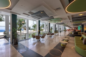 Um hall amplo com design moderno, apresentando áreas de estar, uma mesa de jantar e grandes janelas com vista para o exterior.