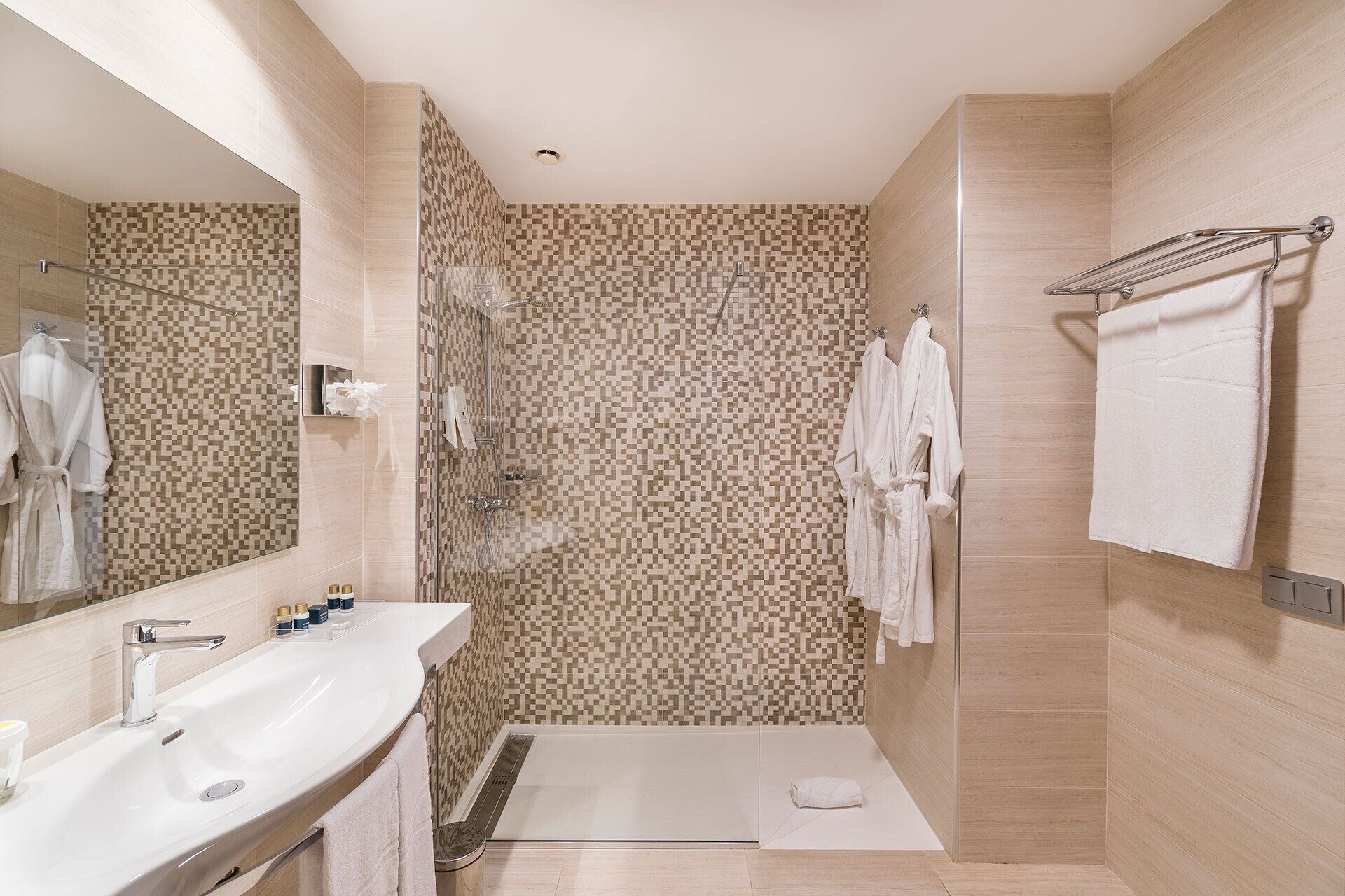 A modern bathroom with a large mirror, a sink, a shower, and a towel rack.