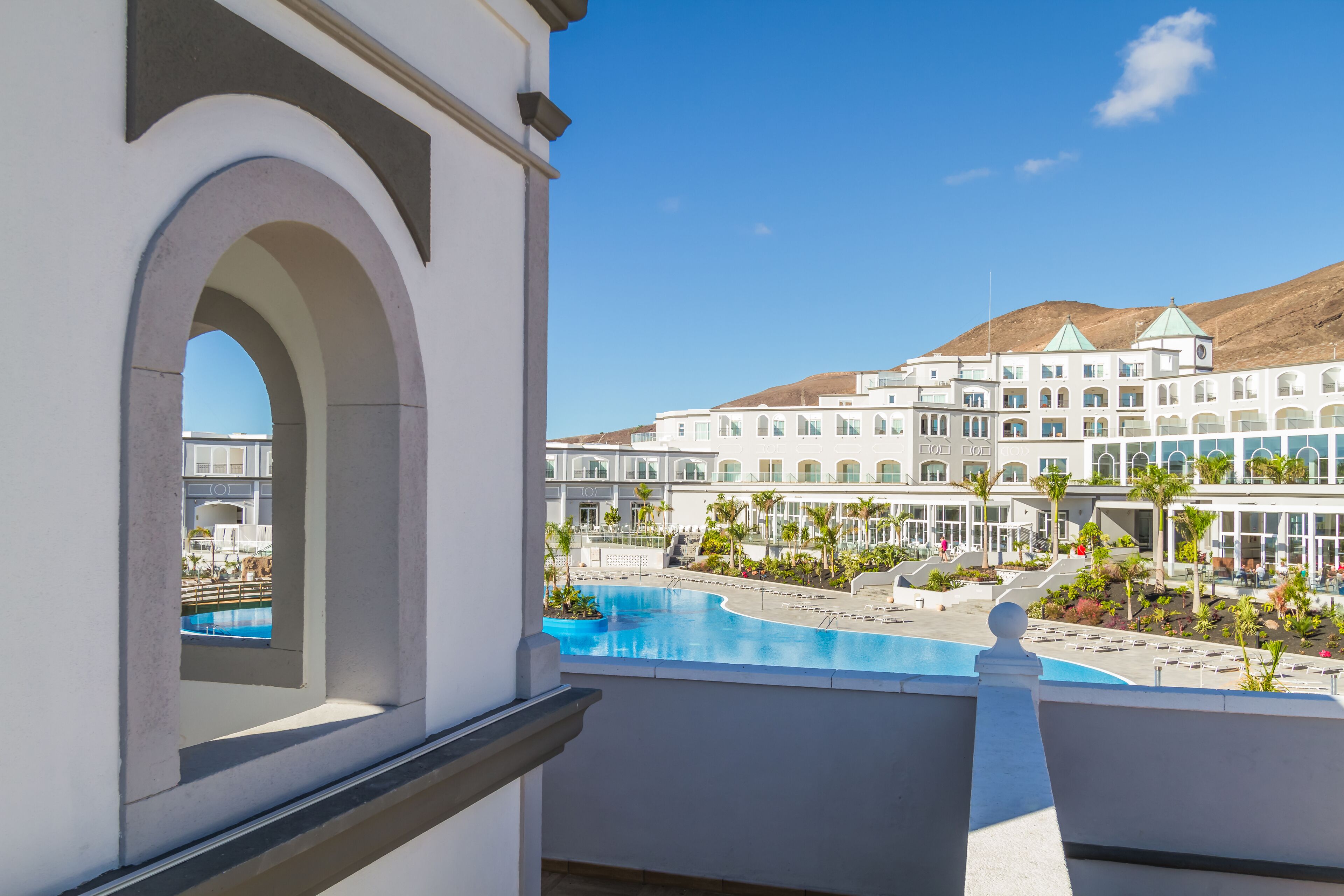 Un hotel con piscina, vista sulle montagne e un edificio alto con diversi piani.