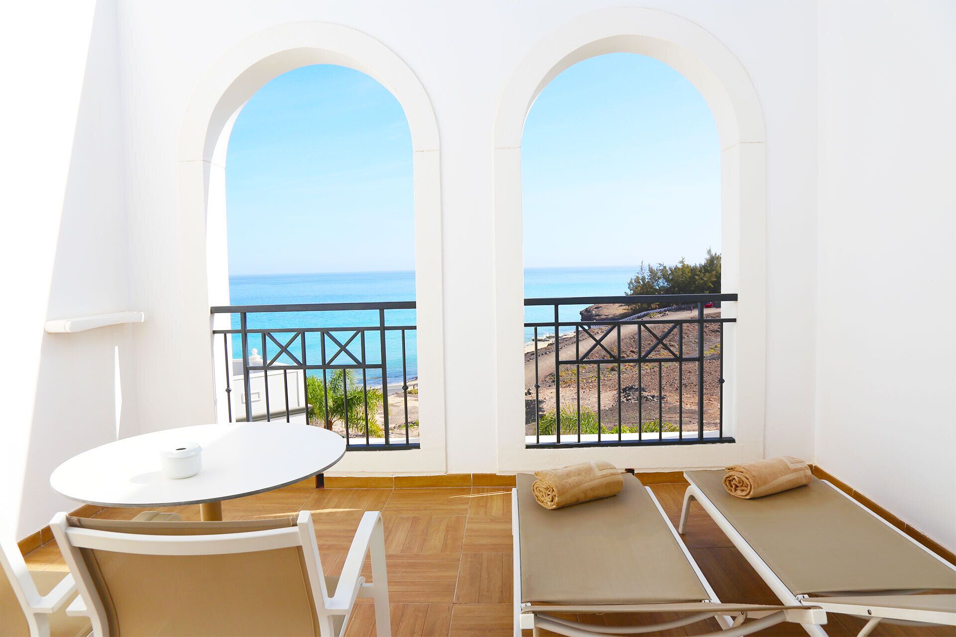 Un balcón con vistas al mar, una mesa, una silla y dos tumbonas.