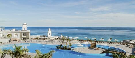 A resort with a large pool, palm trees, and a view of the ocean.