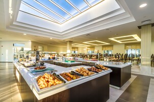 A modern hotel dining area with a buffet setup, skylights, and a spacious layout.