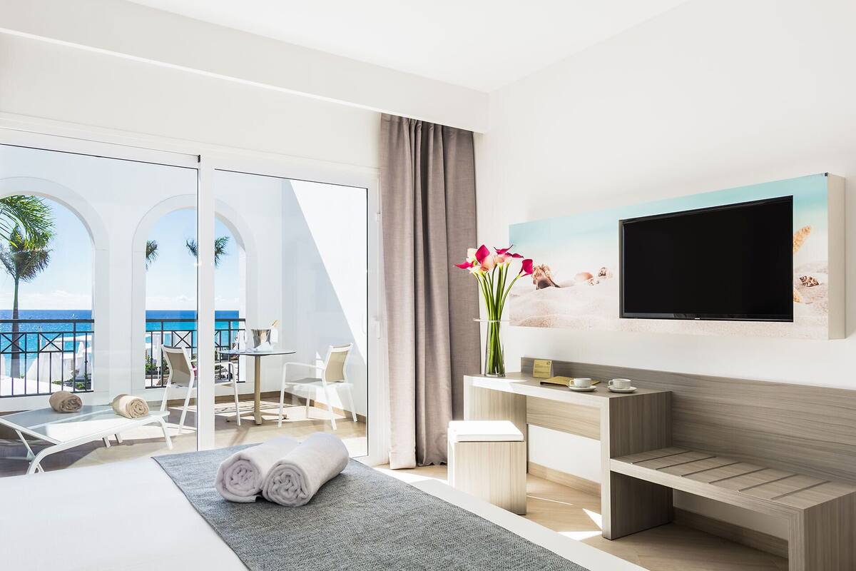 A modern hotel room with a balcony, a TV, a desk, and a bed.