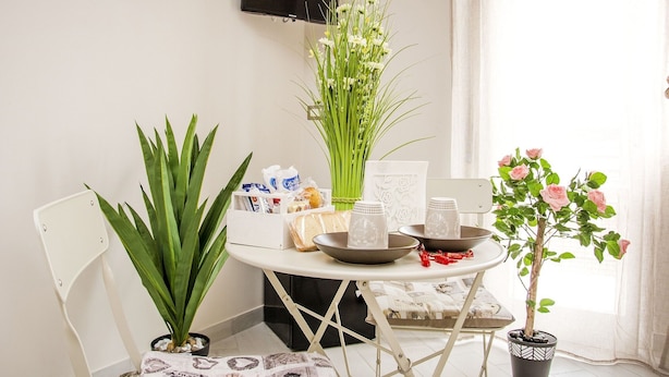Un pequeño comedor con una mesa preparada para dos personas, que incluye una planta en maceta, un jarrón con flores y un plato decorativo.