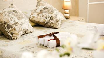 A neatly made bed with patterned pillows and rolled towels, a bedside lamp, and a floral arrangement.
