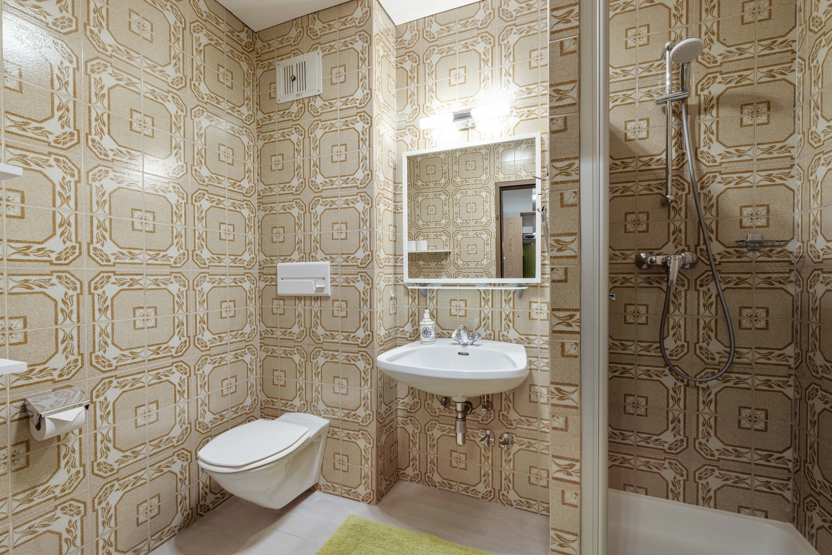 Une salle de bain avec des murs à motifs, un lavabo blanc, des toilettes et une douche.