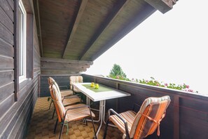 A wooden balcony with a table and chairs, a view of the sky, and a flower border.