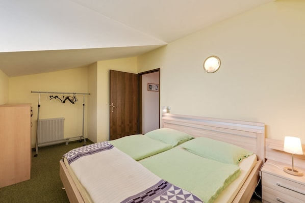 Ein Schlafzimmer mit zwei Betten, einem Kleiderschrank, einem Heizkörper, einem Kleiderständer und einer Nachttischlampe.