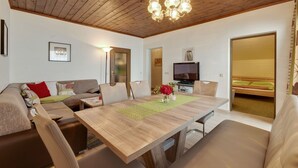 Ein modernes Wohnzimmer mit Holzboden, einem Esstisch, Sofas und einem Fernseher.