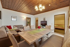 Ein modernes Wohnzimmer mit Holzboden, einem Esstisch, Sofas und einem Fernseher.