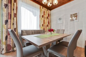 A dining area with a wooden table, cushioned chairs, a vase with flowers, and a window with curtains.