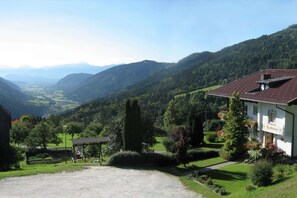 Ein Gebäude mit rotem Ziegeldach, umgeben von üppigem Grün und Bergen im Hintergrund.