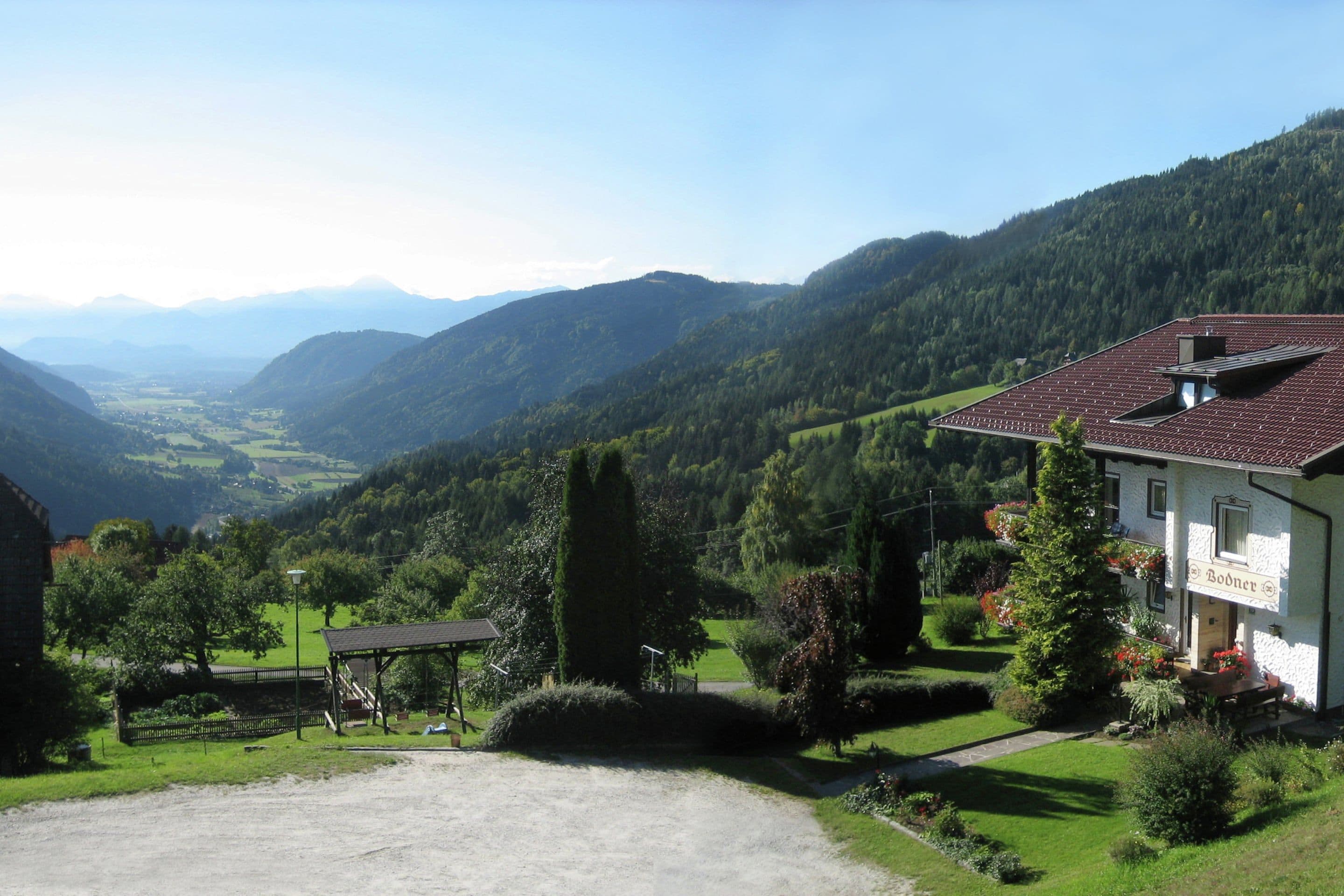 Un bâtiment coiffé d’un toit recouvert de tuiles rouges, entouré d’une végétation luxuriante et avec des montagnes en arrière-plan.