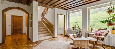 A spacious living area with a wooden staircase, a large window with a view of the outdoors, and a cozy seating area with a patterned rug.