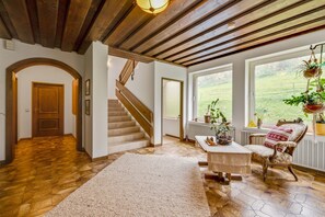 A spacious living area with a wooden staircase, a large window with a view of the outdoors, and a cozy seating area with a patterned rug. - Spacious Apartment in Afritz am See near Ski Area (Treffen)