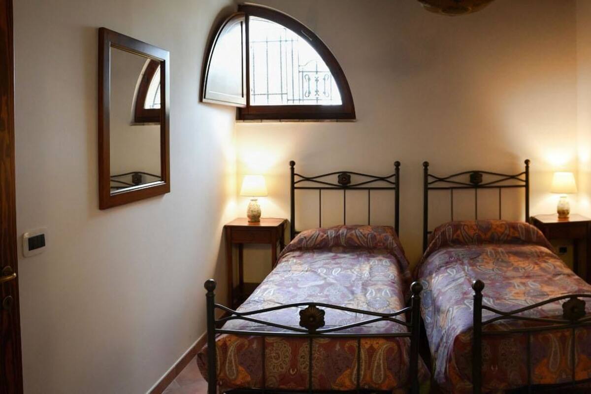 A bedroom with two beds, a window, and a mirror.