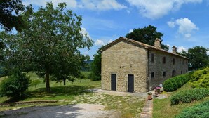 A stone building with a small porch and a door, surrounded by greenery and trees. - Le Case (Pietralunga)