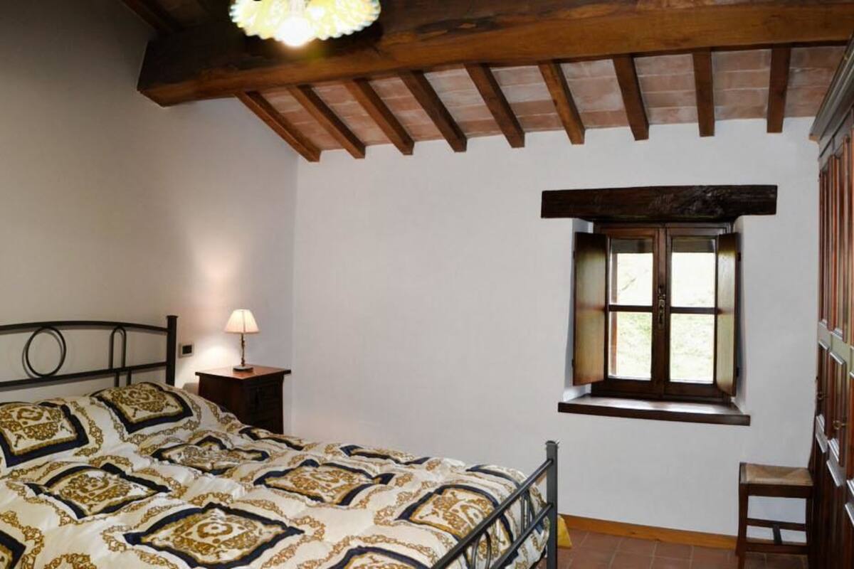 A bedroom with a bed, bedside lamps, a window, and a wooden ceiling.