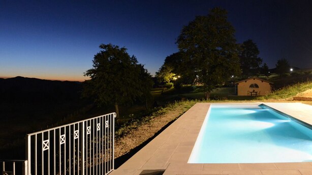 A swimming pool at dusk with surrounding trees and a small building. - Le Case (Pietralunga)