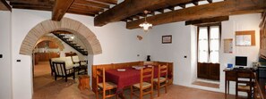 A dining area with a red tablecloth, wooden chairs, and a brick archway leading to a kitchen. - Le Case (Pietralunga)