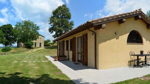 A small building with a tiled roof, a stone wall, and a paved patio with a table and chairs. - Le Case (Pietralunga)