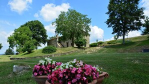 A stone building with a staircase leading up to it, surrounded by lush greenery and flowering plants. - Le Case (Pietralunga)