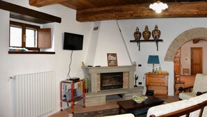 A cozy living room with a fireplace, a bookshelf, and a wooden ceiling. - Le Case (Pietralunga)