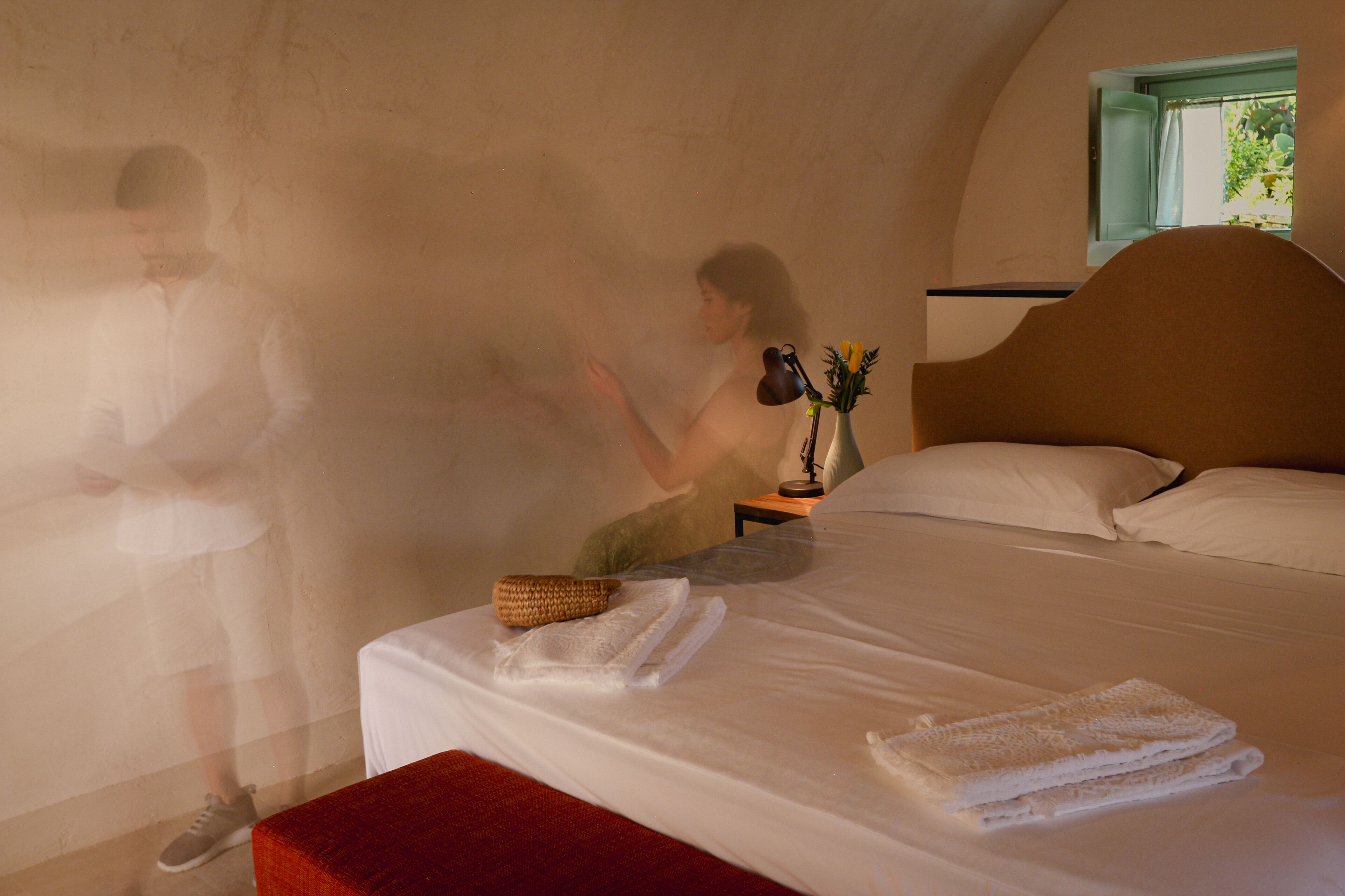 Ein Schlafzimmer mit Bett, Kissen, einem Nachttisch mit Lampe und einem Fenster.