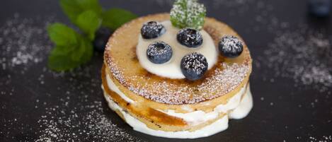 A stack of pancakes with blueberries and powdered sugar on a dark surface.