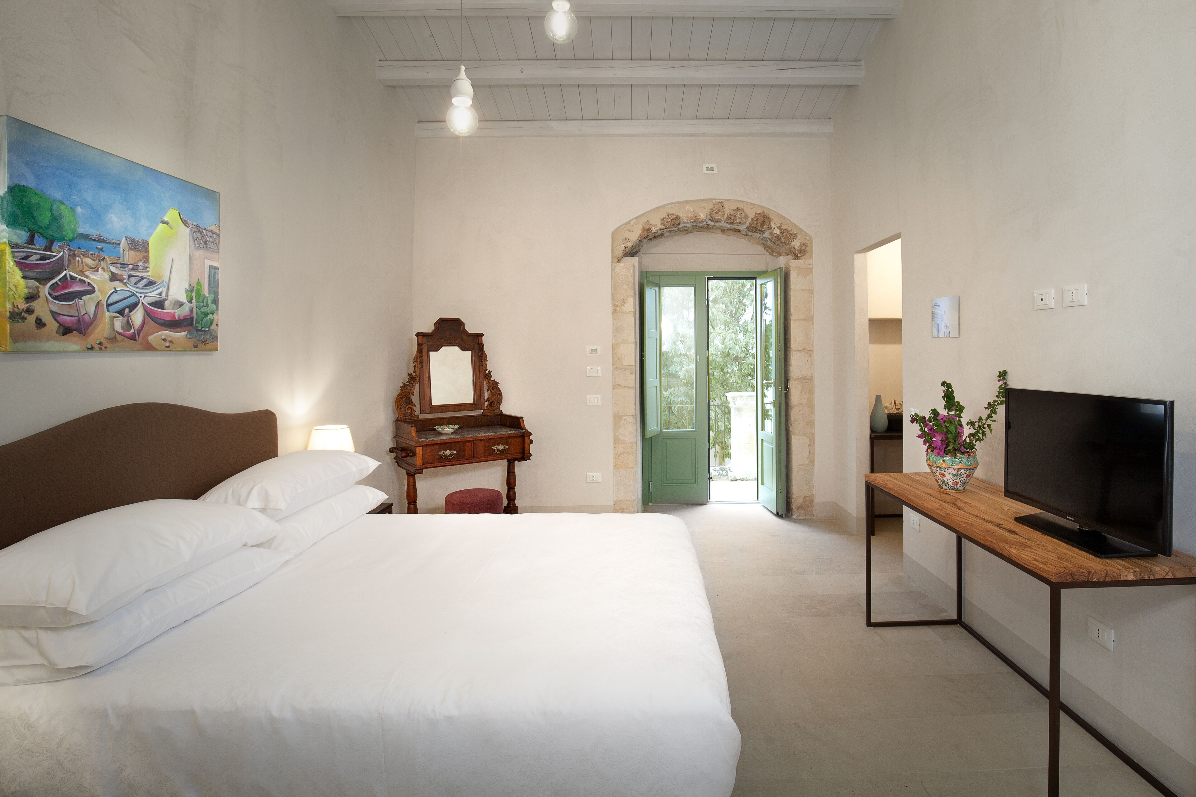 Un dormitorio con una cama, un aparador, un televisor sobre una mesa de madera y un cuadro en la pared.