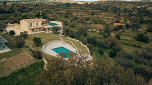A large house with a swimming pool surrounded by a fence, set in a rural landscape with hills in the background. - Terre di Romanello Relais in Val di Noto (Noto)