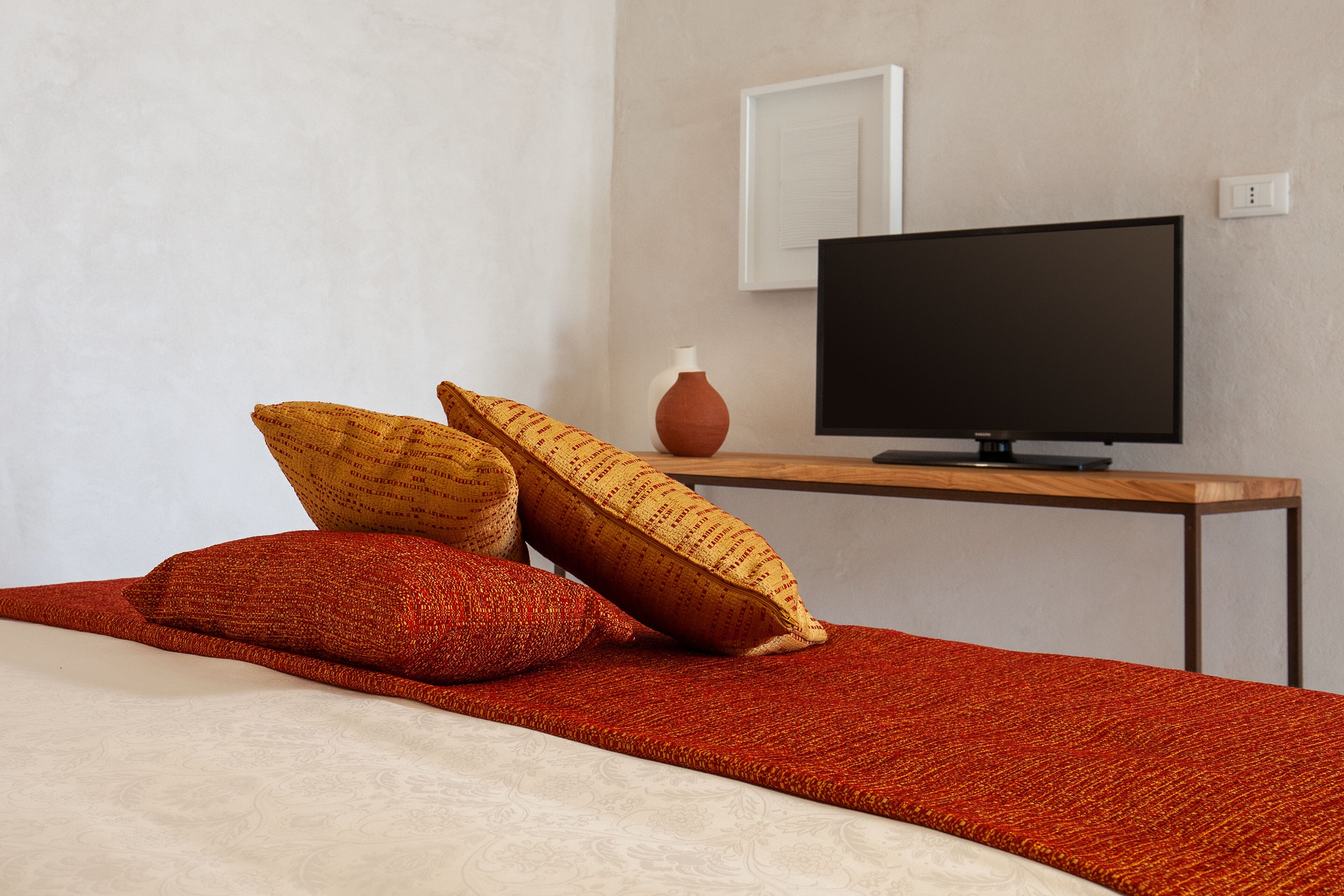 Een slaapkamer met een bed, twee kussens, een televisie op een houten dressoir en een vaas op het dressoir.