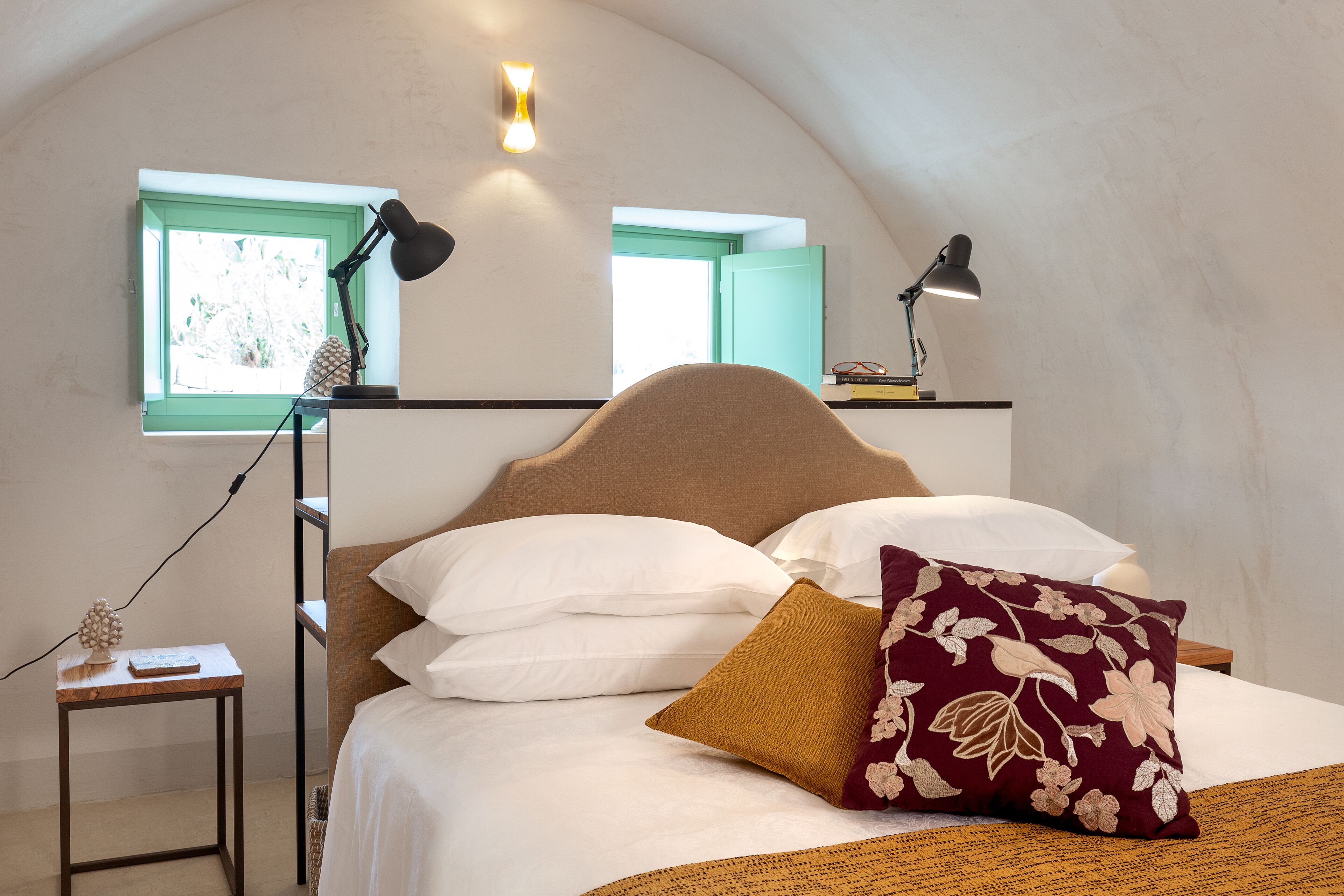 Un dormitorio con cama, almohadas, una mesita de noche, una lámpara y una ventana.