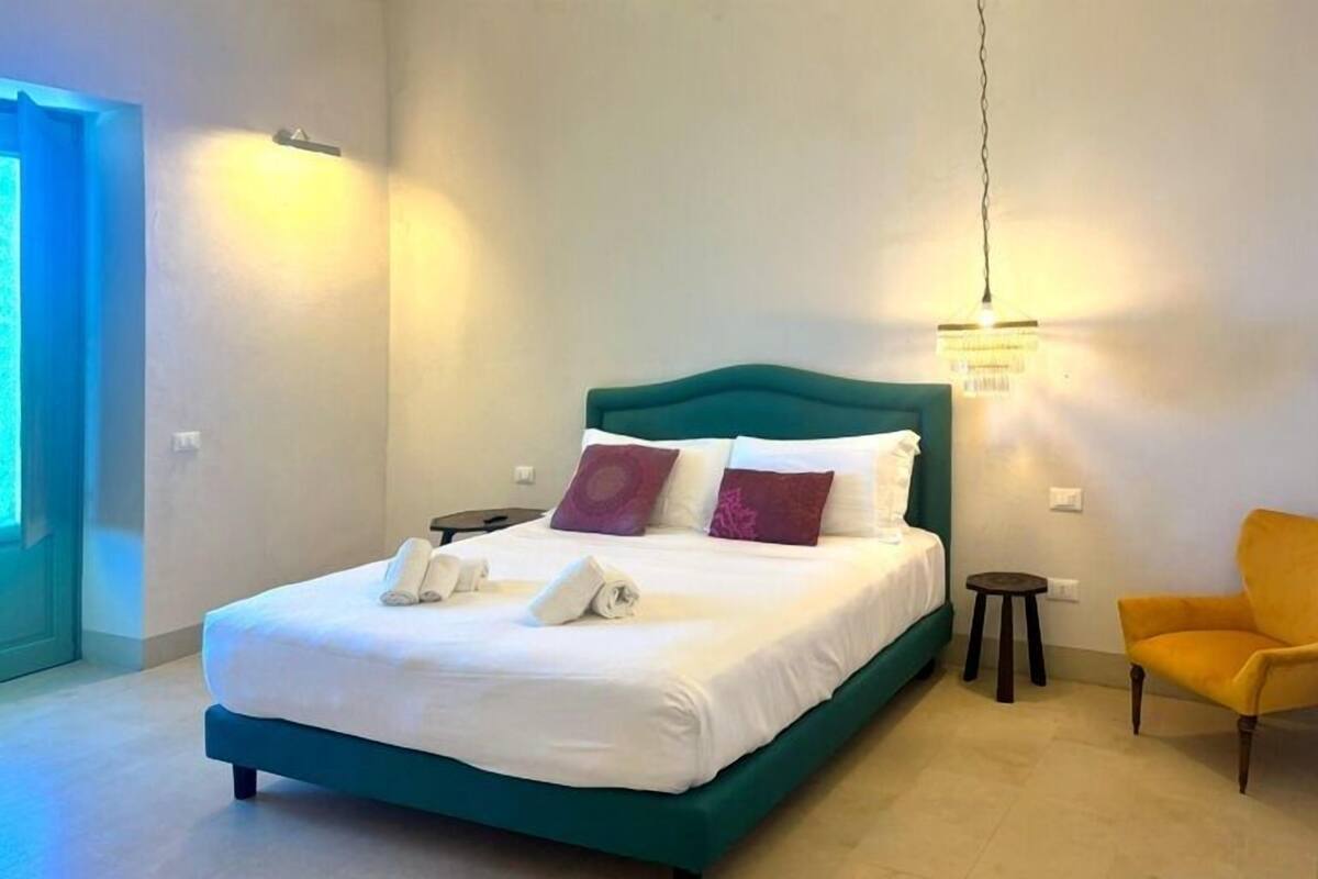 Un dormitorio con una cama color turquesa, ropa de cama blanca y un sillón amarillo.