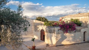 A courtyard with a building, potted plants, and a clear sky. - Terre di Romanello Relais in Val di Noto (Noto)