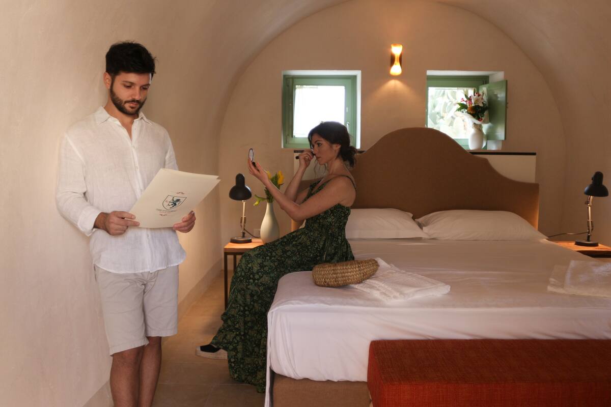 Habitación de hotel con cama, mesita de noche con lámpara y ventana con vistas.