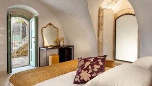 A bedroom with a bed, a desk, a mirror, and a view of a stone staircase. - Terre di Romanello Relais in Val di Noto (Noto)