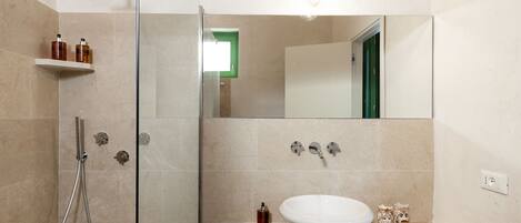 Un baño moderno con ducha de vidrio, un espejo grande y un lavabo con pileta blanca.