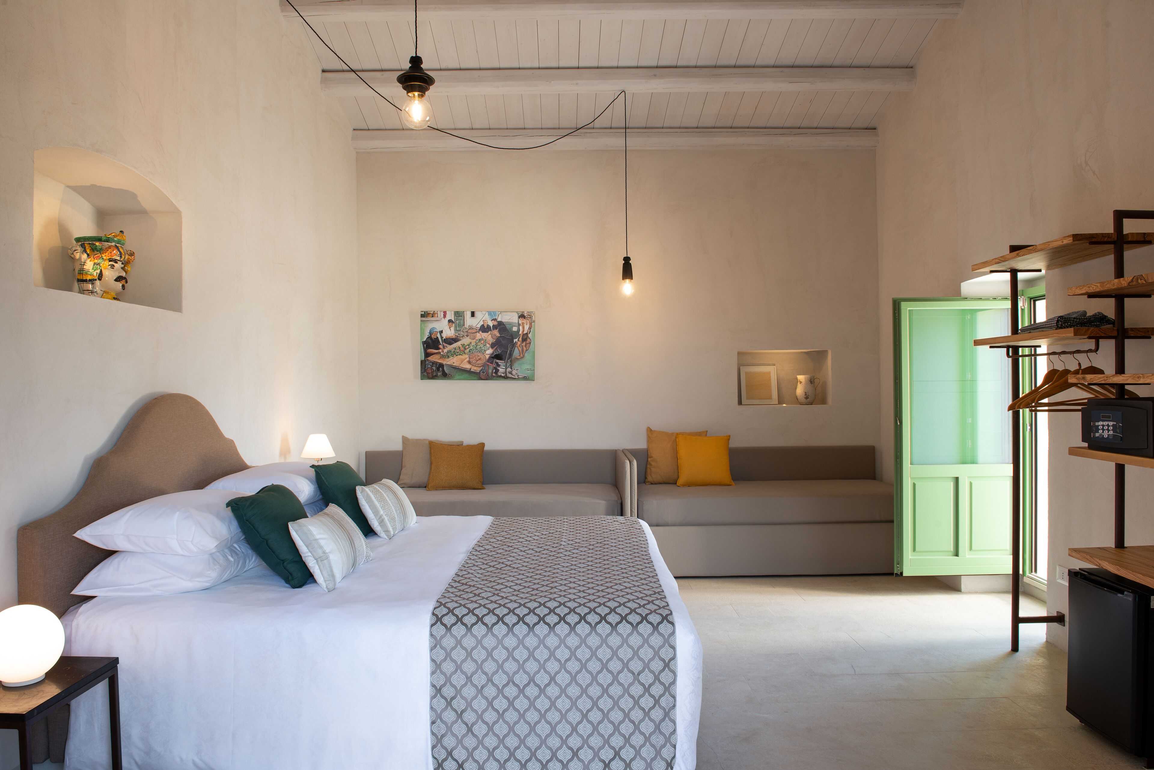 A bedroom with a large bed, a sofa, a green door, and a wall-mounted shelf with shoes.