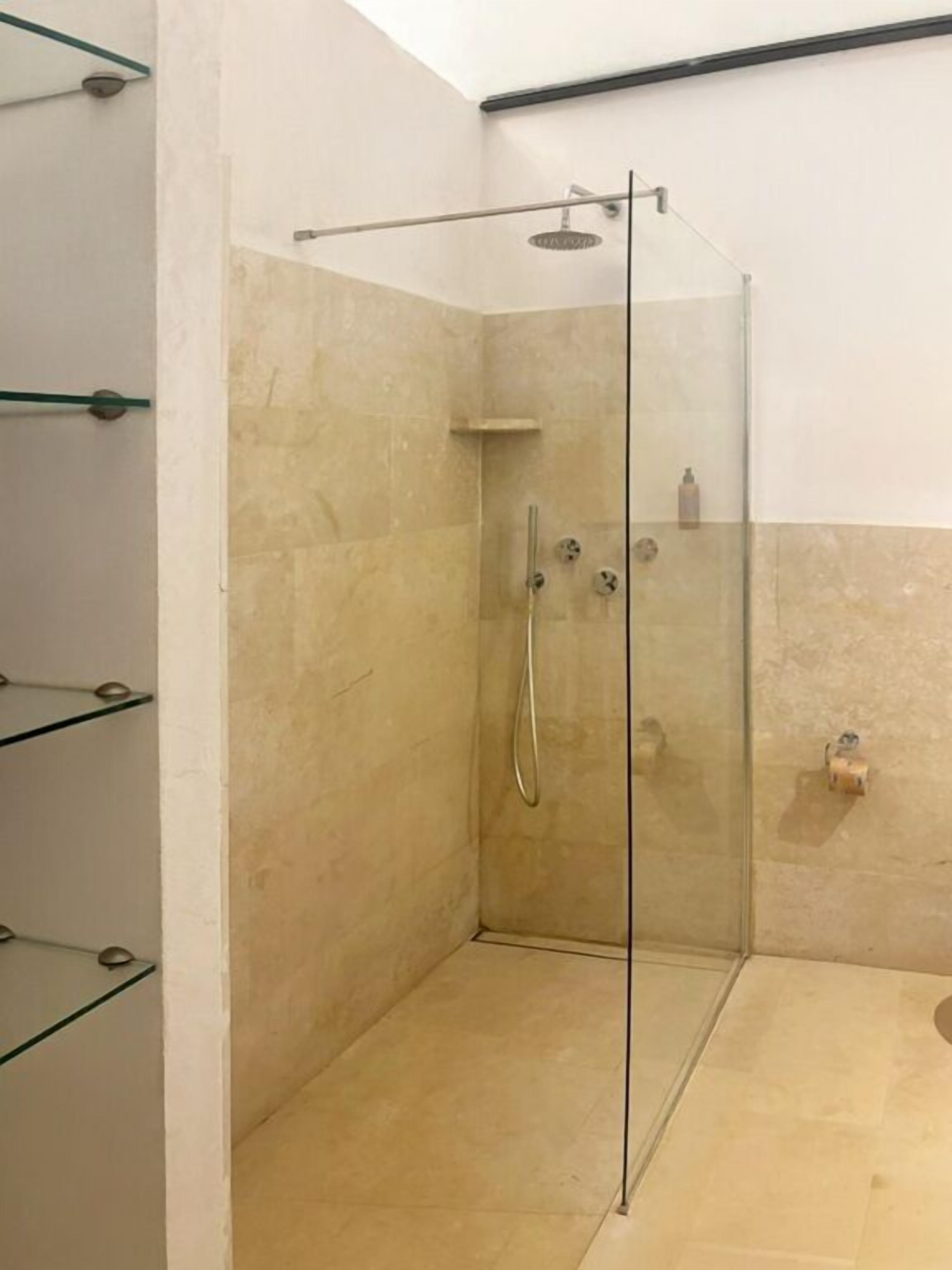 A glass-enclosed shower with a handheld showerhead, a wall-mounted faucet, and a small shelf with toiletries.